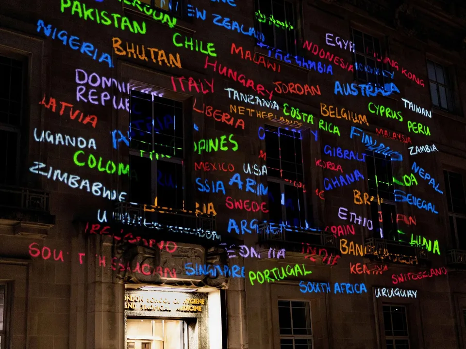 building front with city names projected on it in multiple colors