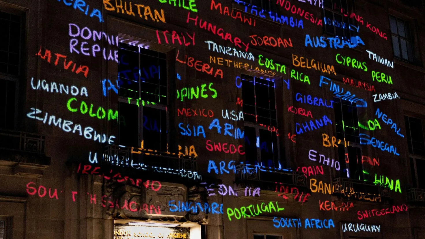 building front with city names projected on it in multiple colors