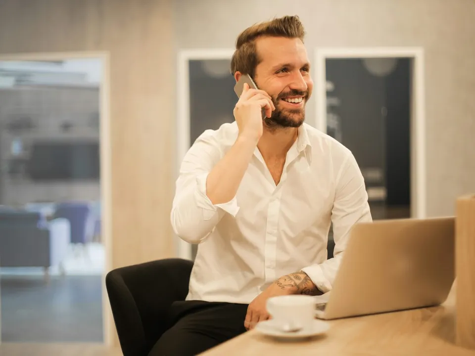 man sitting calling with a phone and looking at a laptop