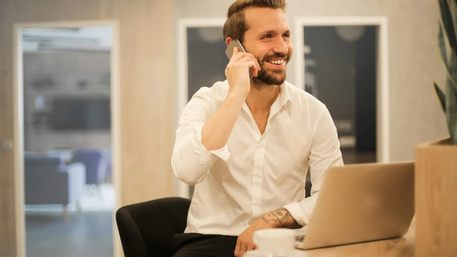 man sitting calling with a phone and looking at a laptop