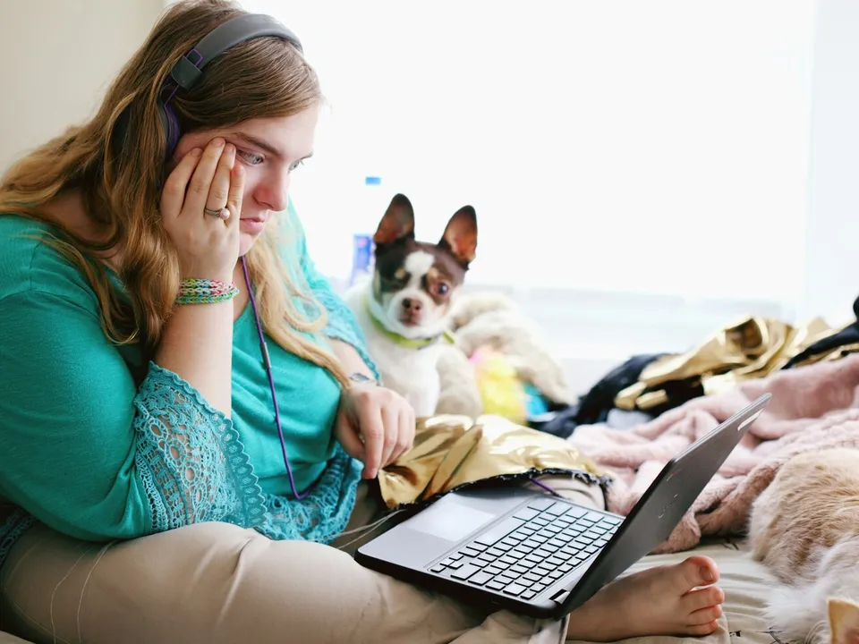 woman sitting on a couch and looking at a laptop with a small dog next to her