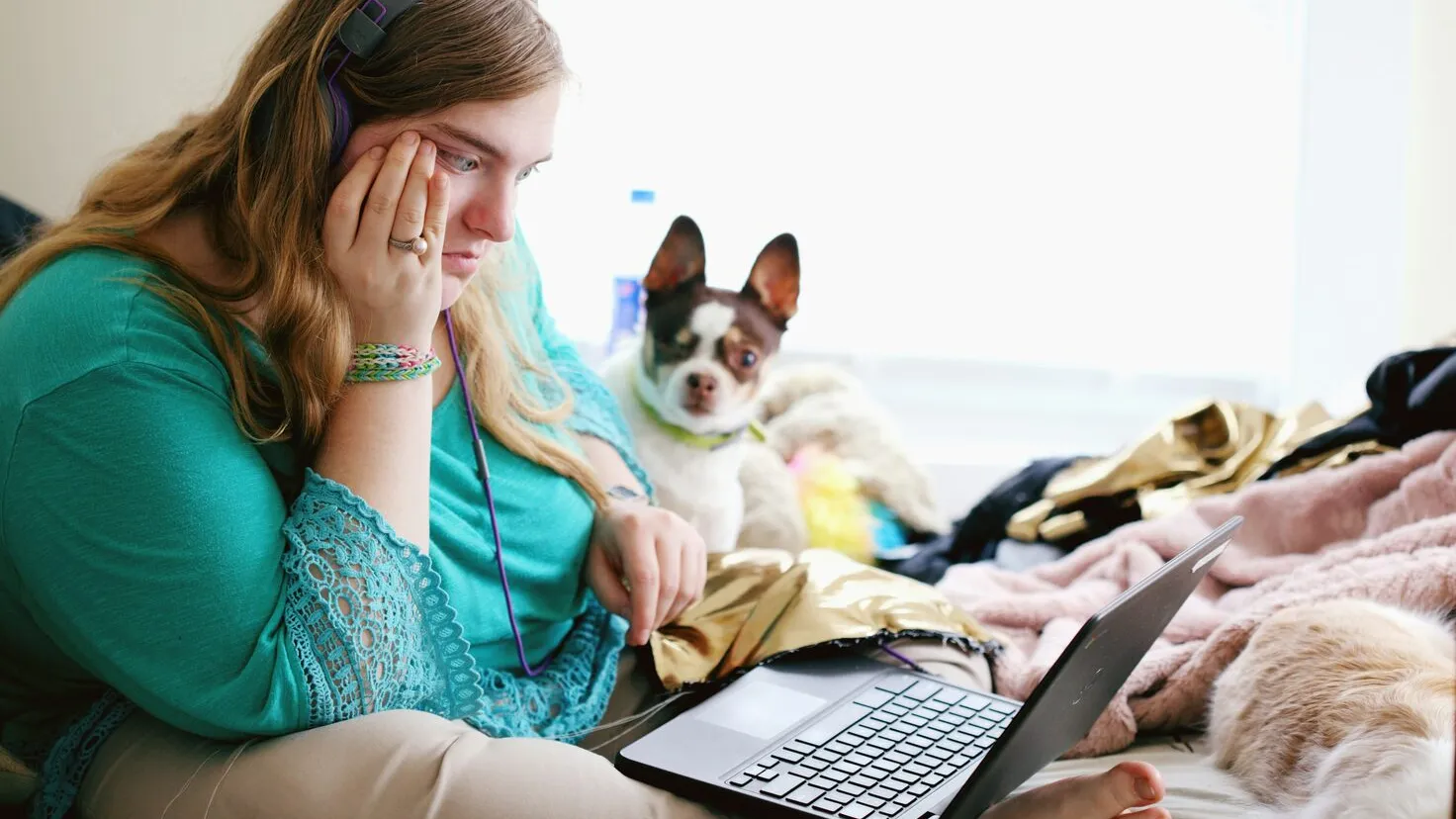 woman sitting on a couch and looking at a laptop with a small dog next to her