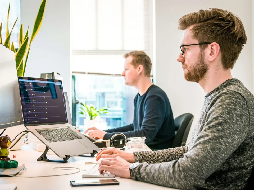 2 men sitting at shared desk looking at their monitors