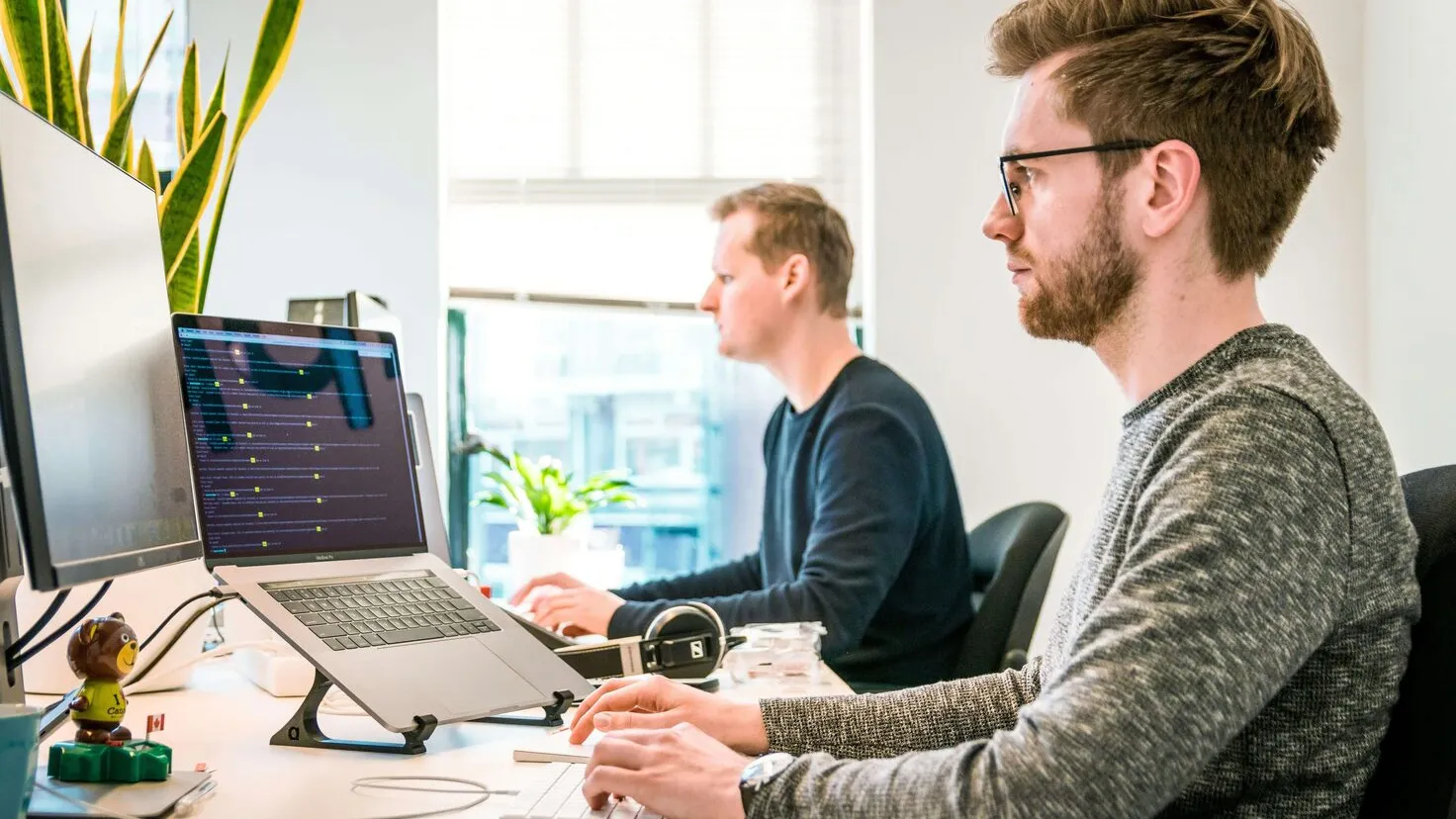 2 men sitting at shared desk looking at their monitors