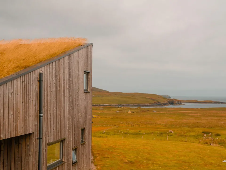 the edge of a building with a grass roof and a body of water in the background