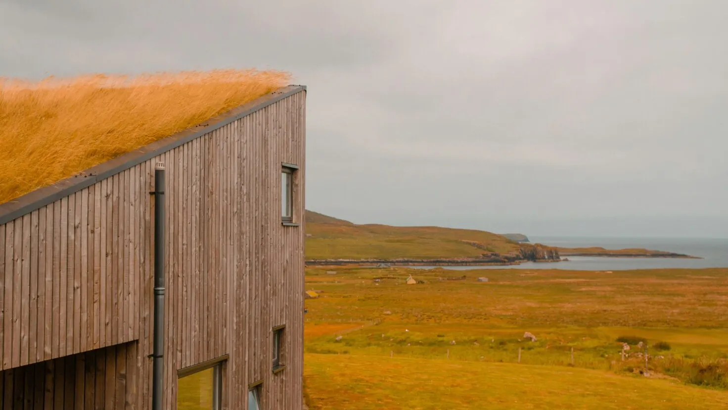 the edge of a building with a grass roof and a body of water in the background