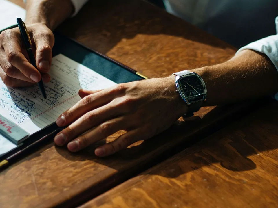 person writing on a paper leaning on a brown table