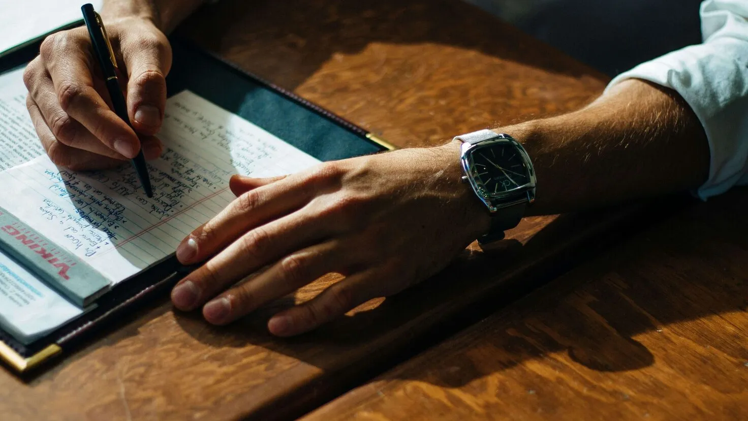 person writing on a paper leaning on a brown table